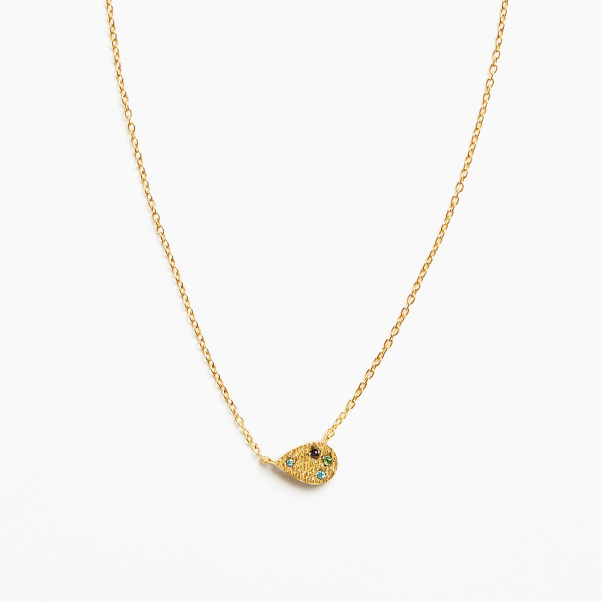 A delicate gold chain necklace featuring a small teardrop-shaped pendant adorned with tiny green and blue stones and a central black detail, set against a plain white background.