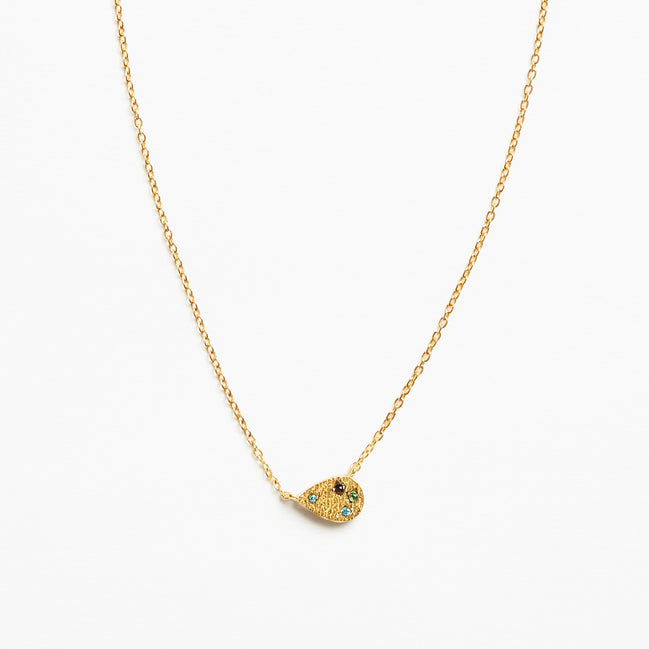 A delicate gold chain necklace featuring a small teardrop-shaped pendant adorned with tiny green and blue stones and a central black detail, set against a plain white background.