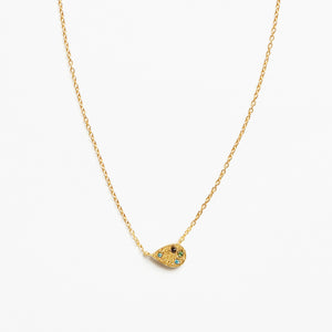 A delicate gold chain necklace featuring a small teardrop-shaped pendant adorned with tiny green and blue stones and a central black detail, set against a plain white background.