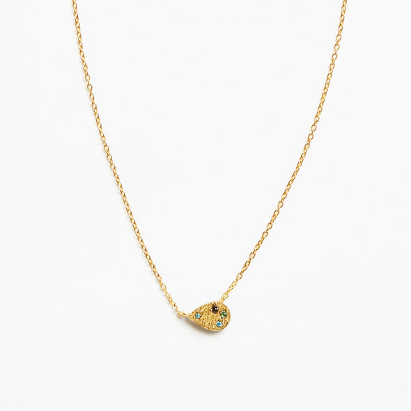 A delicate gold chain necklace featuring a small teardrop-shaped pendant adorned with tiny green and blue stones and a central black detail, set against a plain white background.